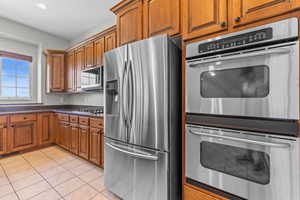 Kitchen with stainless steel appliances, brown cabinetry, light tile patterned flooring, and recessed lighting