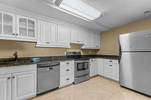 Kitchen with appliances with stainless steel finishes, white cabinetry, light tile patterned flooring, glass insert cabinets, and a textured ceiling