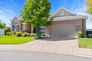 View of front of house with stone siding, driveway, an attached garage, and a front lawn