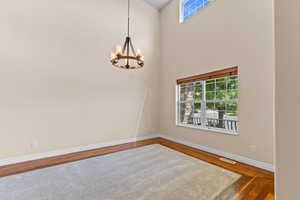Unfurnished room featuring wood finished floors, a chandelier, and a towering ceiling