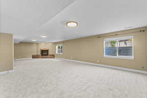 Unfurnished living room featuring light colored carpet, a tiled fireplace, and a textured ceiling
