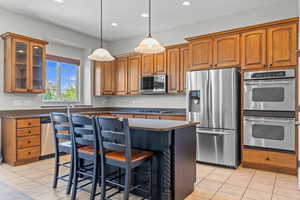 Kitchen featuring a kitchen bar, appliances with stainless steel finishes, a center island, light tile patterned flooring, and pendant lighting