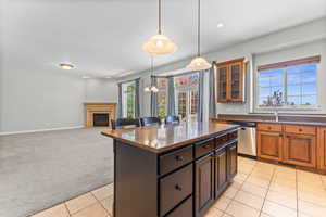 Kitchen featuring light carpet, pendant lighting, a glass covered fireplace, dishwasher, and dark stone counters