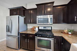 Kitchen with stainless steel appliances, light stone counters, light tile patterned flooring, and dark brown cabinetry