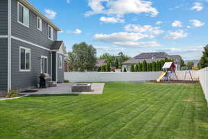 Fenced backyard with a playground, a patio area, and an outdoor fire pit