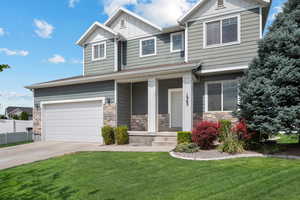 Craftsman-style home with board and batten siding, driveway, a front yard, a porch, and a garage