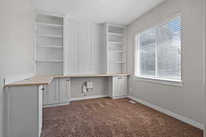 Unfurnished office featuring built in study area and dark colored carpet