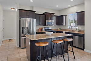 Kitchen with dark brown cabinetry, stainless steel appliances, a kitchen bar, a center island, and light tile patterned flooring