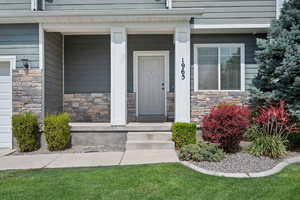 Entrance to property featuring stone siding, covered porch, and a garage