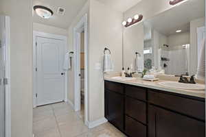 Bathroom featuring a shower stall, light tile patterned floors, and double vanity
