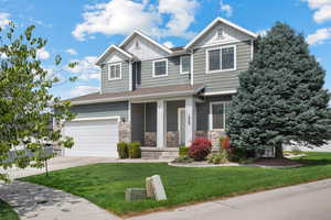 Craftsman-style house featuring board and batten siding, concrete driveway, a front lawn, stone siding, and a porch