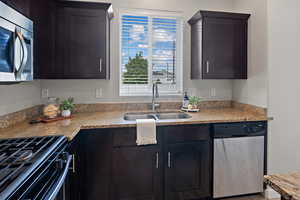 Kitchen with stainless steel appliances, light stone counters, and dark brown cabinetry
