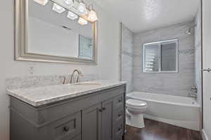 Bathroom featuring shower / bathtub combination, vanity, dark wood-type flooring, and a textured ceiling