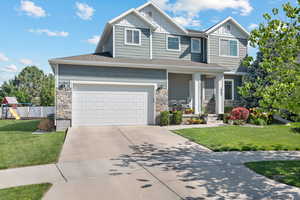 Craftsman house with board and batten siding, stone siding, concrete driveway, a playground, and a garage
