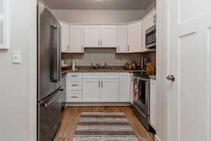 Kitchen with light wood-style flooring, white cabinetry, dark stone counters, and appliances with stainless steel finishes