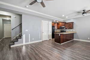 Kitchen with a ceiling fan, ornamental molding, light stone counters, a peninsula, and dark wood finished floors