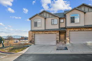 View of front facade with a garage, board and batten siding, driveway, stone siding, and stucco siding