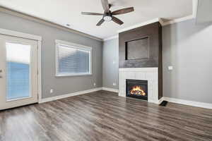 Unfurnished living room with crown molding, a tile fireplace, dark wood-type flooring, and ceiling fan