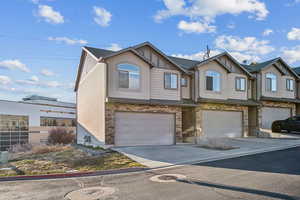 View of front of house featuring a garage, driveway, stone siding, and a residential view