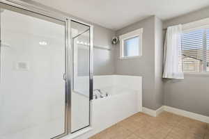 Full bathroom featuring light tile patterned flooring, a stall shower, and a garden tub