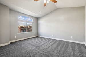 Empty room featuring vaulted ceiling, dark carpet, and ceiling fan