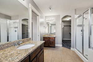 Bathroom featuring a spacious closet, a shower stall, two vanities, and light tile patterned floors