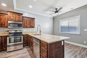 Kitchen with ornamental molding, stainless steel appliances, light stone countertops, a peninsula, and light wood-style flooring