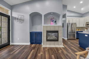 Unfurnished living room with a tiled fireplace, dark wood-style flooring, lofted ceiling, and recessed lighting