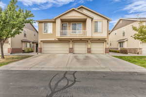 View of front of property featuring a balcony, stucco siding, a garage, driveway, and brick siding
