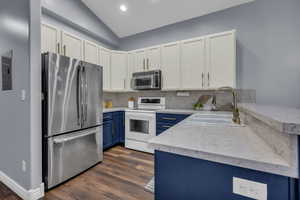 Kitchen with blue cabinets, white cabinetry, stainless steel appliances, light stone countertops, and decorative backsplash