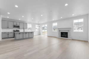 Kitchen with gray cabinets, light countertops, open floor plan, recessed lighting, and a kitchen island with sink