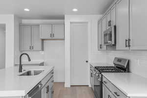 Kitchen with gray cabinets, stainless steel appliances, backsplash, light wood-style flooring, and recessed lighting