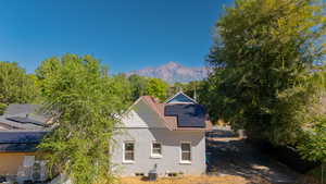 Back of house featuring roof mounted solar panels, stucco siding, a mountain view, and a shingled roof