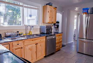 Kitchen featuring stainless steel appliances, light brown cabinets, dark stone countertops, light tile patterned floors, and tasteful backsplash