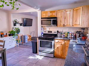 Kitchen with appliances with stainless steel finishes, decorative backsplash, dark stone countertops, light brown cabinetry, and a chandelier