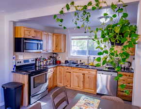 Kitchen featuring stainless steel appliances, dark tile patterned flooring, dark stone counters, and light brown cabinets