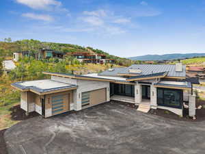 Contemporary house featuring a standing seam roof, driveway, a metal roof, stone siding, and a garage