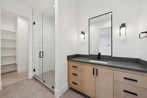 Full bath featuring light tile patterned floors, vanity, a stall shower, and a spacious closet