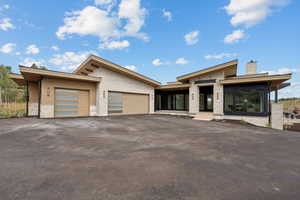 Contemporary home featuring driveway, a garage, a chimney, and stone siding