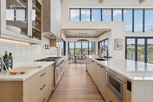 Kitchen with light stone countertops, light brown cabinetry, stainless steel appliances, a large island, and a towering ceiling