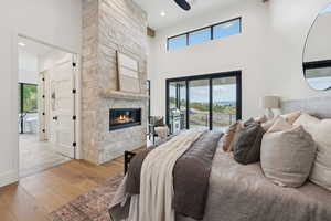 Bedroom with light wood-style flooring, access to exterior, a high ceiling, a stone fireplace, and a ceiling fan