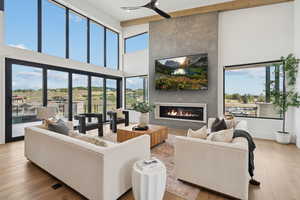Living room with light wood finished floors, a fireplace, a towering ceiling, and a ceiling fan
