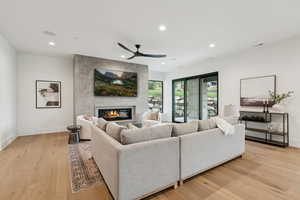 Living area with a glass covered fireplace, recessed lighting, light wood-type flooring, and a ceiling fan