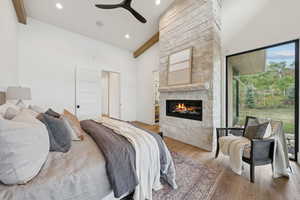 Bedroom with high vaulted ceiling, wood finished floors, beam ceiling, a fireplace, and ceiling fan