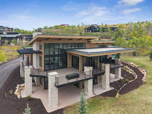 Back of house with a patio, stone siding, a standing seam roof, a metal roof, and a balcony