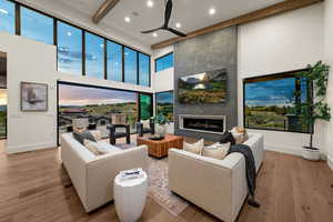 Living room with a large fireplace, light wood-style floors, recessed lighting, beamed ceiling, and a high ceiling