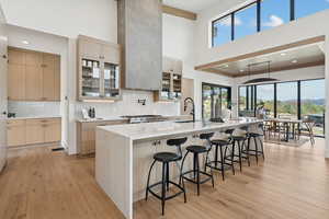 Kitchen featuring glass insert cabinets, a kitchen breakfast bar, light brown cabinets, light wood finished floors, and a high ceiling