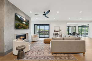 Living area featuring light wood finished floors, recessed lighting, a glass covered fireplace, and a ceiling fan