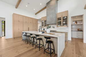 Kitchen with glass insert cabinets, a kitchen bar, light brown cabinets, high vaulted ceiling, and backsplash