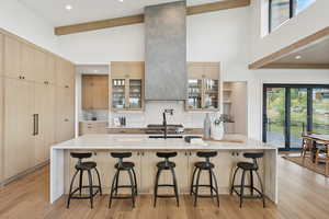 Kitchen featuring light brown cabinetry, a large island, decorative backsplash, a breakfast bar, and beam ceiling